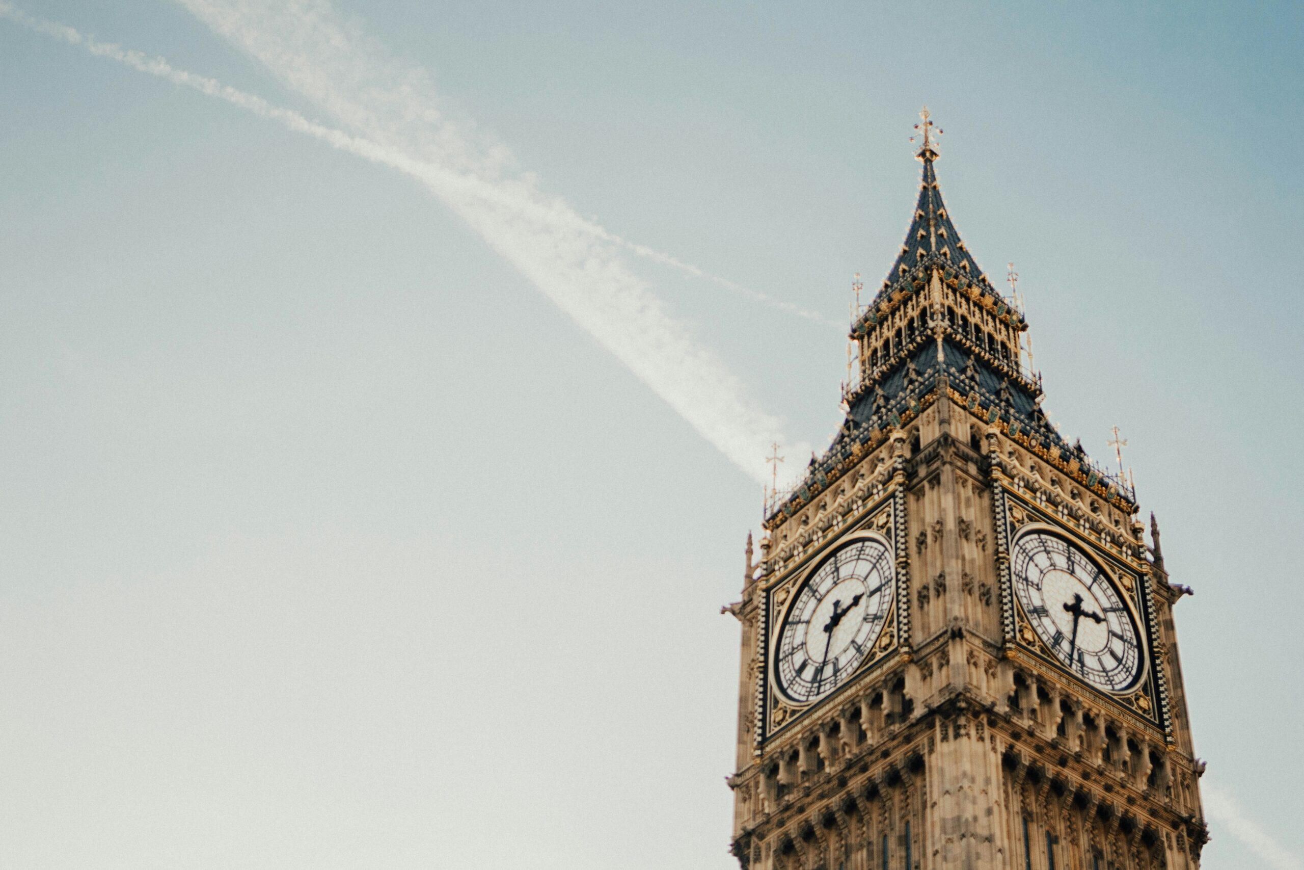 Big Ben Clock Tower, London – A close-up view of the Elizabeth Tower, commonly known as Big Ben, against a clear sky with diagonal contrails. The intricate Gothic Revival architecture and ornate clock faces stand out, making it one of London’s most iconic landmarks.